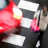 Movimiento borroso de un auto rojo y un peatón cruzando la calle.