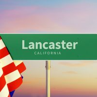 Lancaster – California. Señal de carretera o de pueblo. Bandera de los Estados Unidos. Cielo al atardecer o al amanecer.