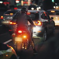 Motociclista espera en tráfico nocturno denso, vehículos en carretera con luces encendidas, ambiente urbano iluminado. Conducción nocturna. Motociclista con equipo completo navegando calle congestionada al atardecer. Motociclista espera en tráfico nocturno denso, vehículos en carretera con luces encendidas, ambiente urbano iluminado. Conducción nocturna. Motociclista con equipo completo navegando calle congestionada al atardecer.