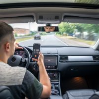 Persona conduciendo mientras usa un teléfono móvil con el velocímetro marcando 57 mph en una carretera despejada Persona conduciendo mientras usa un teléfono móvil con el velocímetro marcando 57 mph en una carretera despejada