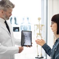 GP showing x-ray on tablet to lady in cervical collar