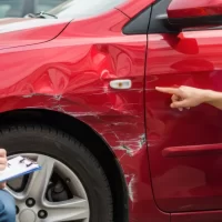 a-man-in-a-blue-shirt-points-at-a-deep-scratch-and-dent-on-a-red-cars-side[1]